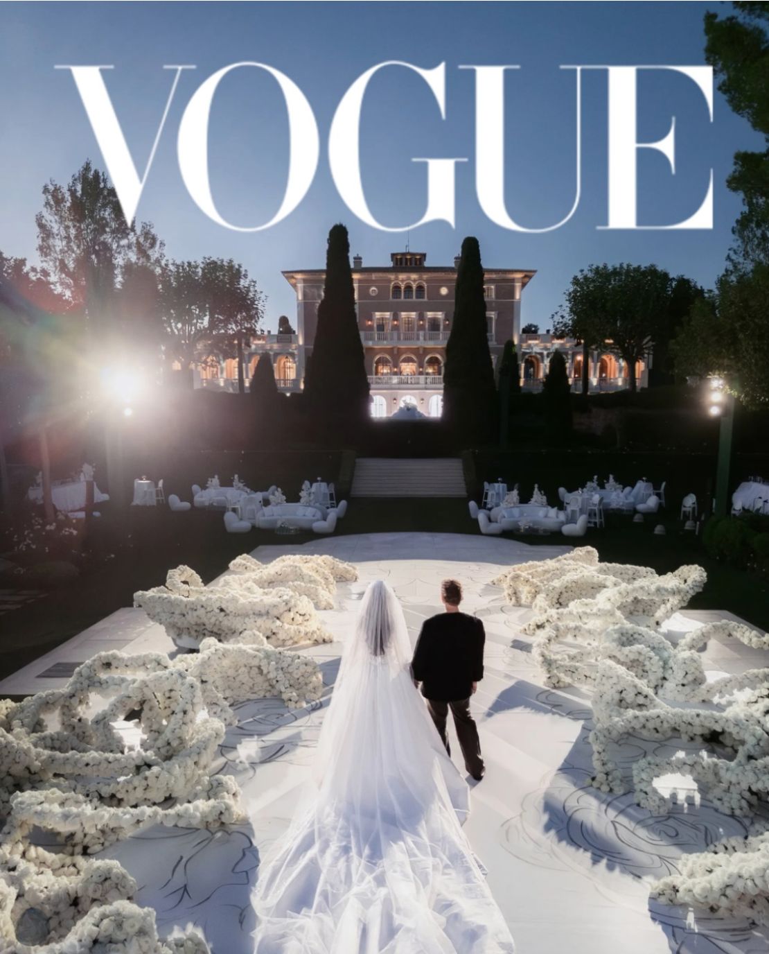 Vogue-featured wedding planned by the Darcy team: bride walking a white floral aisle towards a villa at dusk